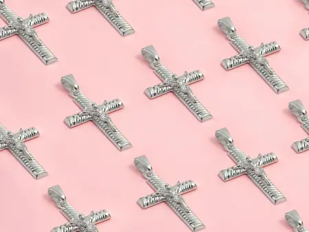 Kolekcija srebrnih privjesaka s križićima raspoređenih na ružičastoj pozadini.